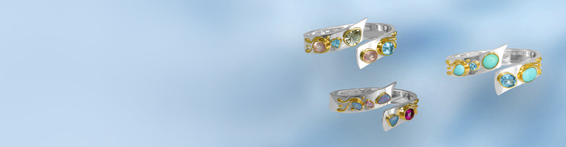 Three silver rings with colorful gemstone clusters, including yellow, green, blue, and red stones, floating against a soft light blue gradient background.