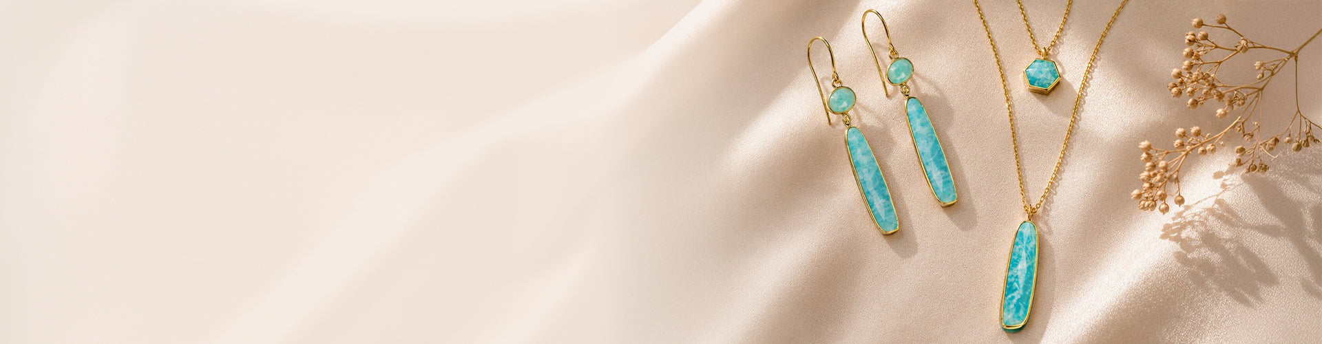 Jorge Revilla turquoise gemstone necklace and drop earrings in gold settings displayed on a soft beige background.