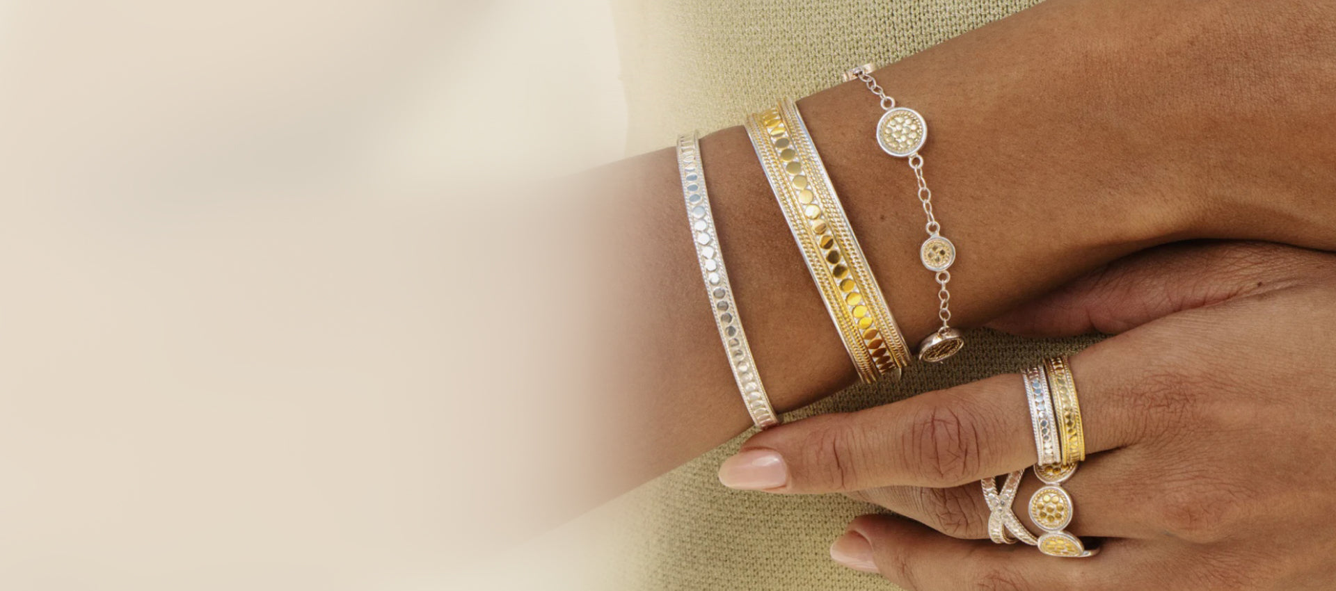 Model wearing mixed-metal gold and silver bracelets and rings with modern textured detailing, styled in a layered jewelry look.